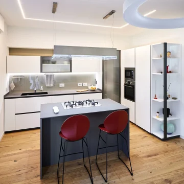 Immagine di una cucina moderna realizzata da Danilo Arredamenti con isola centrale con fuochi e sgabelli rossi